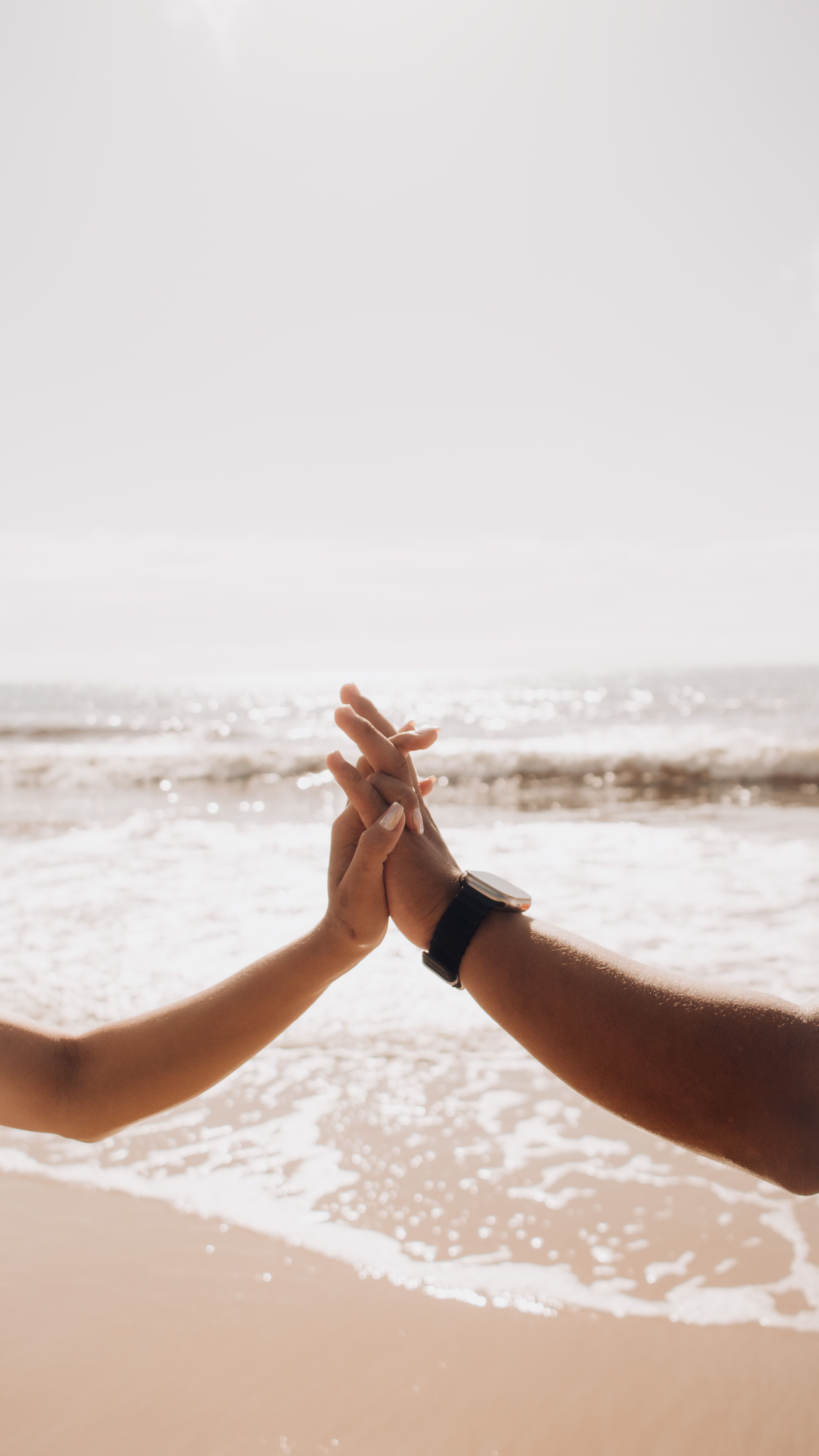 Silhouettes of a couple holding hands by the sea on a bright sunny day, symbolizing love.