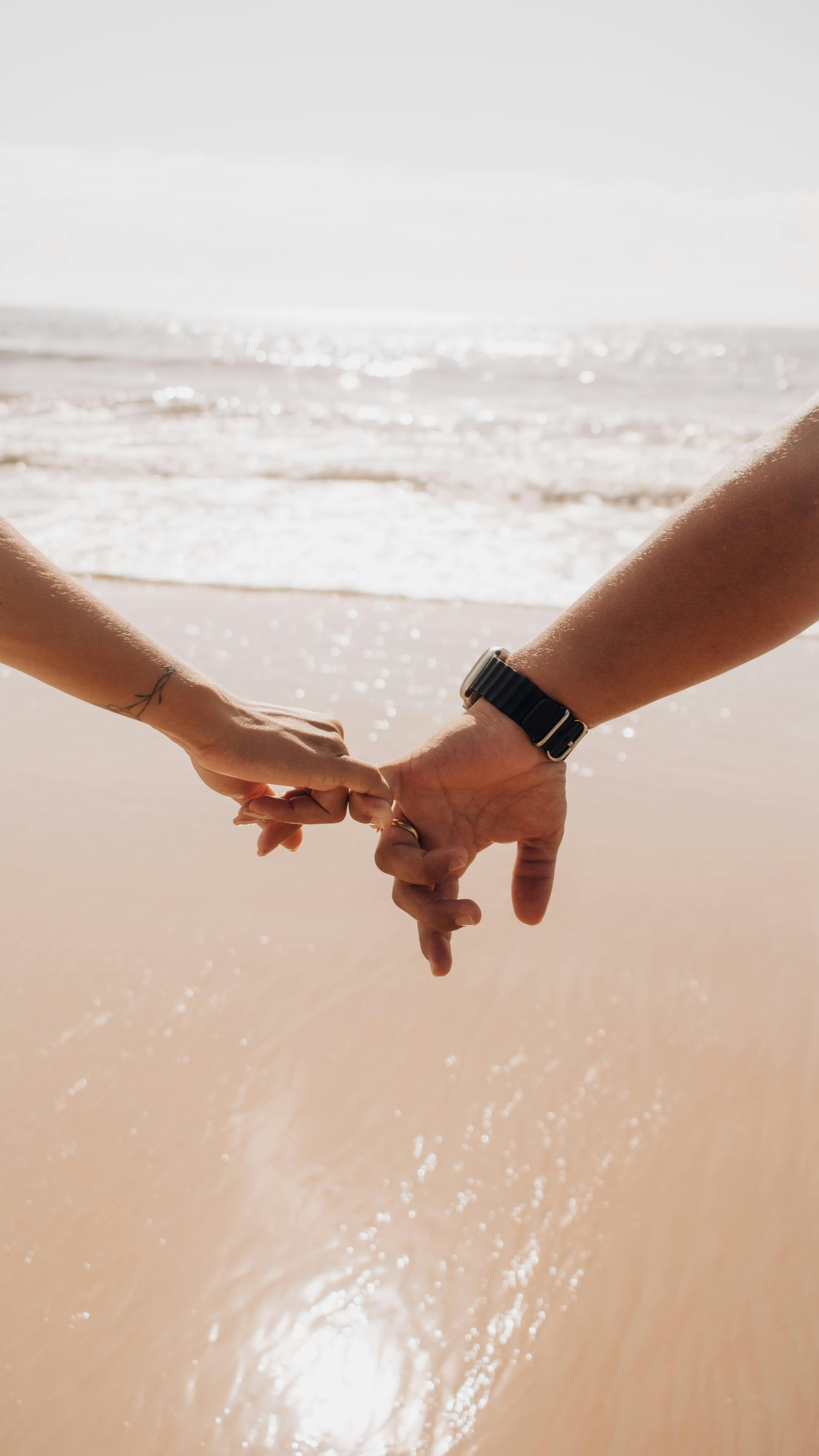 A couple holding hands at a beach, symbolizing love and connection on a sunny day.