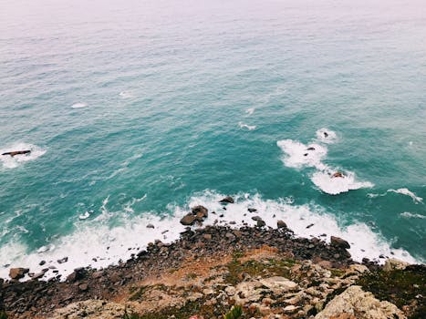 A stunning aerial view of the rocky coastline in Portugal with turquoise waves crashing against the shore.