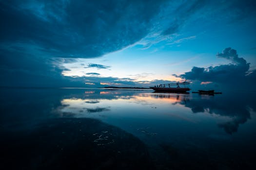 Serene ocean view in Bali at sunset with a silhouetted boat and dramatic skies.
