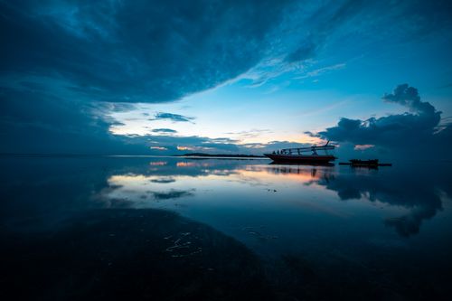Free Serene ocean view in Bali at sunset with a silhouetted boat and dramatic skies. Stock Photo
