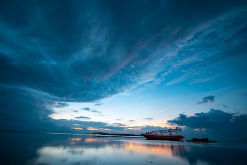 Free A serene boat floats on calm waters in Bali, Indonesia against a dramatic dusk sky. Stock Photo