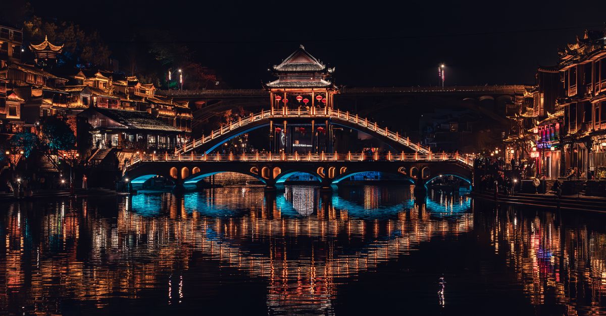 Stunning night view of Fenghuang Bridge in Xiangxi, China, with vibrant reflections.