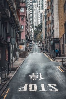 A narrow urban alley in a bustling city with high-rise buildings and a distinctive stop sign.