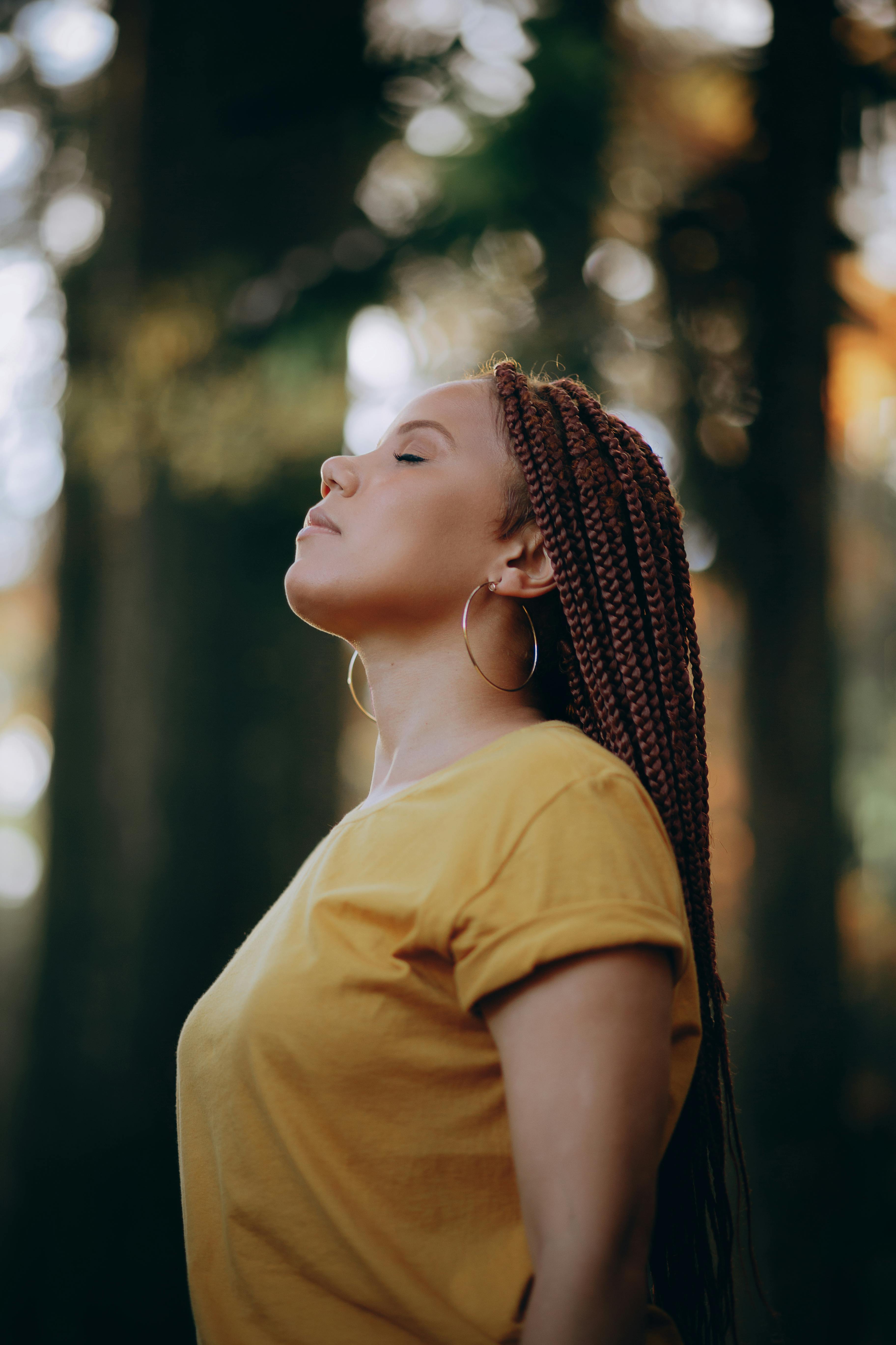 A peaceful woman with braided hair enjoys the outdoors, eyes closed in relaxation.