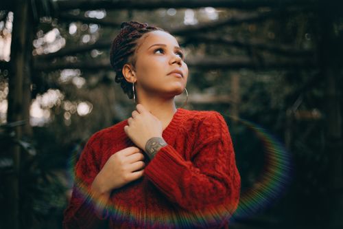 Free Portrait of a woman with braided hair in a red sweater, looking thoughtfully to the side outdoors. Stock Photo