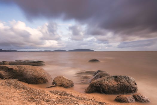Panoramic view of a tranquil beach in Porto Alegre, Brazil, with rocks and a moody sky.