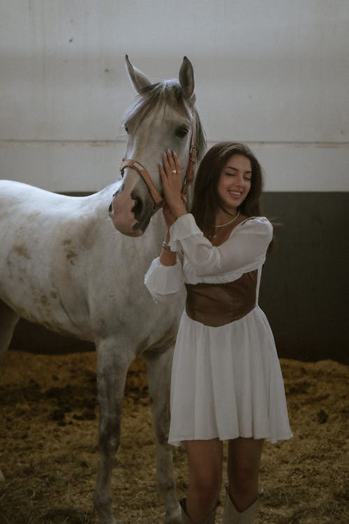 A woman in a white dress is petting a horse