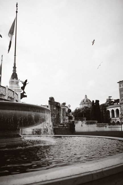 Black and white photo of a historic fountain in Rome, Italy, with architectural details and urban setting.