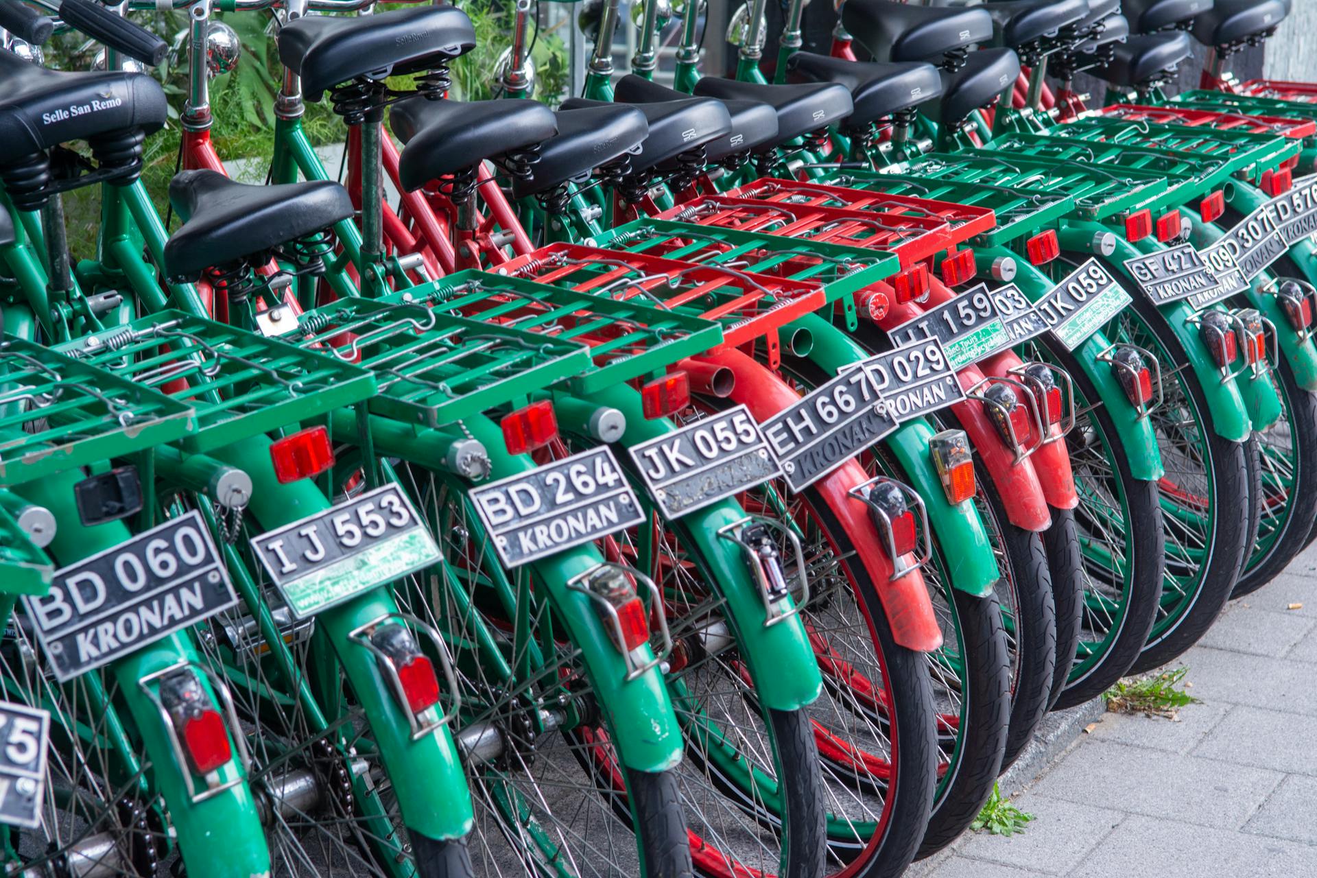 Vibrant green and red rental bicycles parked in a neat row with license plates.