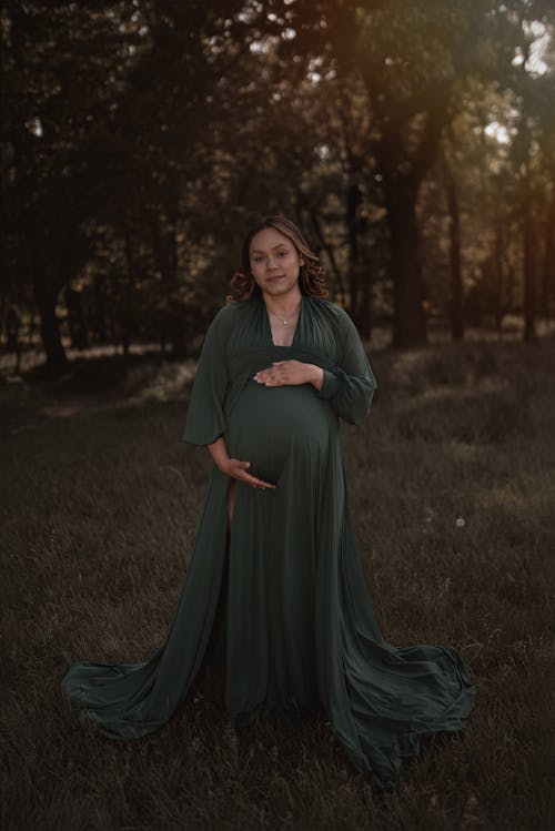 A pregnant woman in a green dress standing in the middle of a field