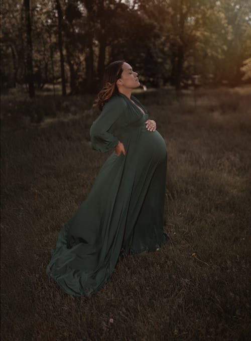 A pregnant woman in a green dress is standing in a field