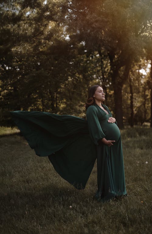 A pregnant woman in a green dress is standing in the middle of a field