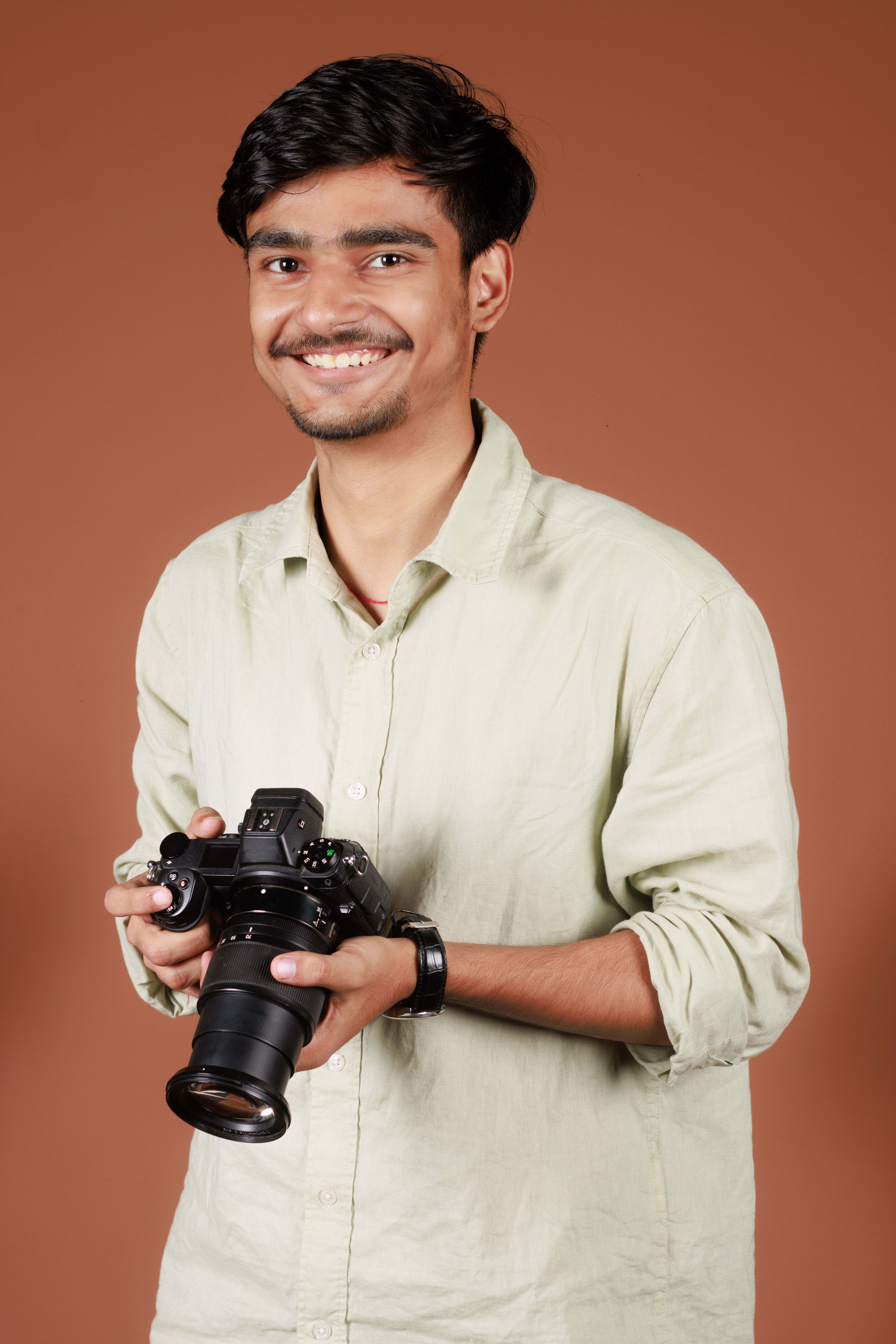 Cheerful young man in a studio holding a professional camera, ready for photoshoot.