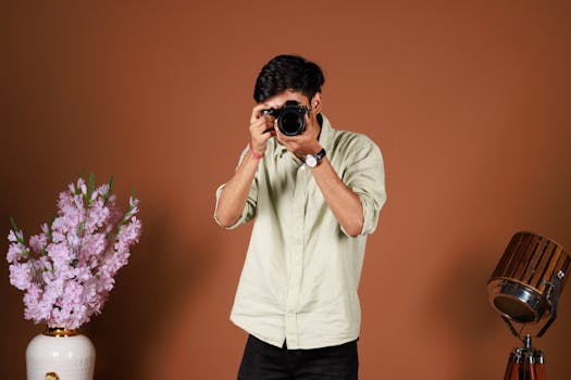 A stylish portrait of a man holding a camera in a studio with flowers.