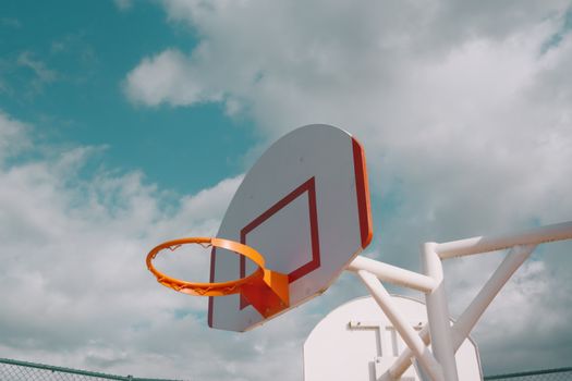 A minimalist view of a basketball hoop against a cloudy sky, highlighting the contrast of vivid colors.