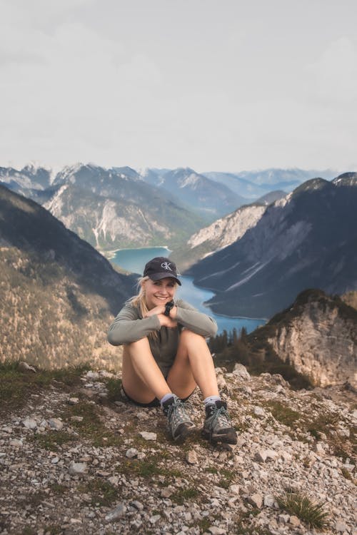 A woman sitting on top of a mountain with a lake in the background