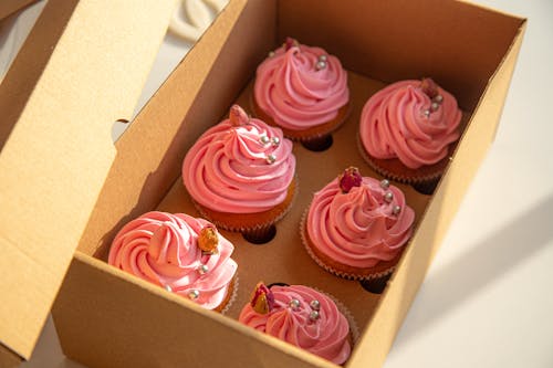 A box of cupcakes with pink frosting and sprinkles