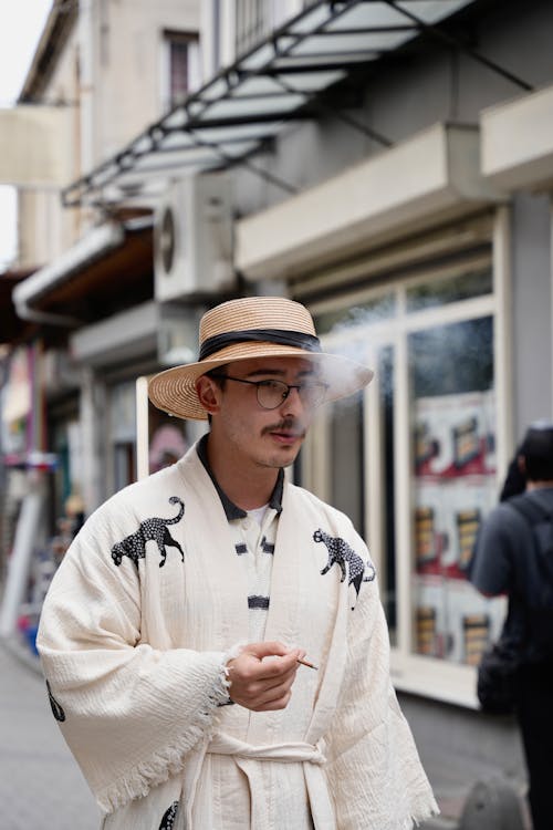 A man in a white hat and a straw hat smoking a cigarette