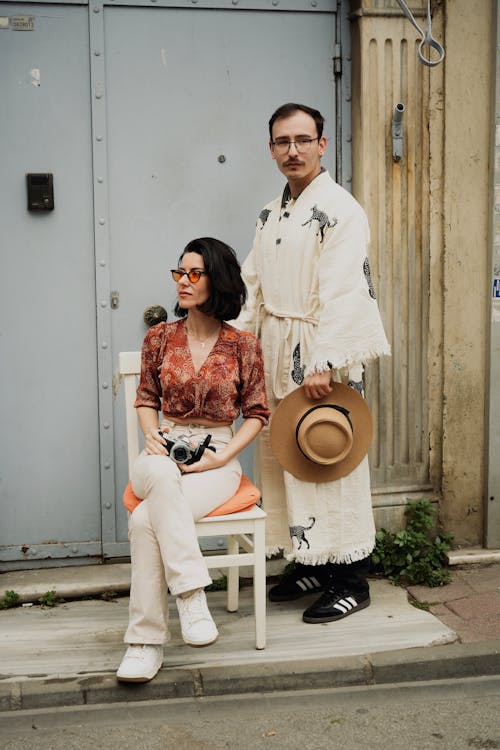 Man in Robes Standing with Hat and Woman Sitting on Chair