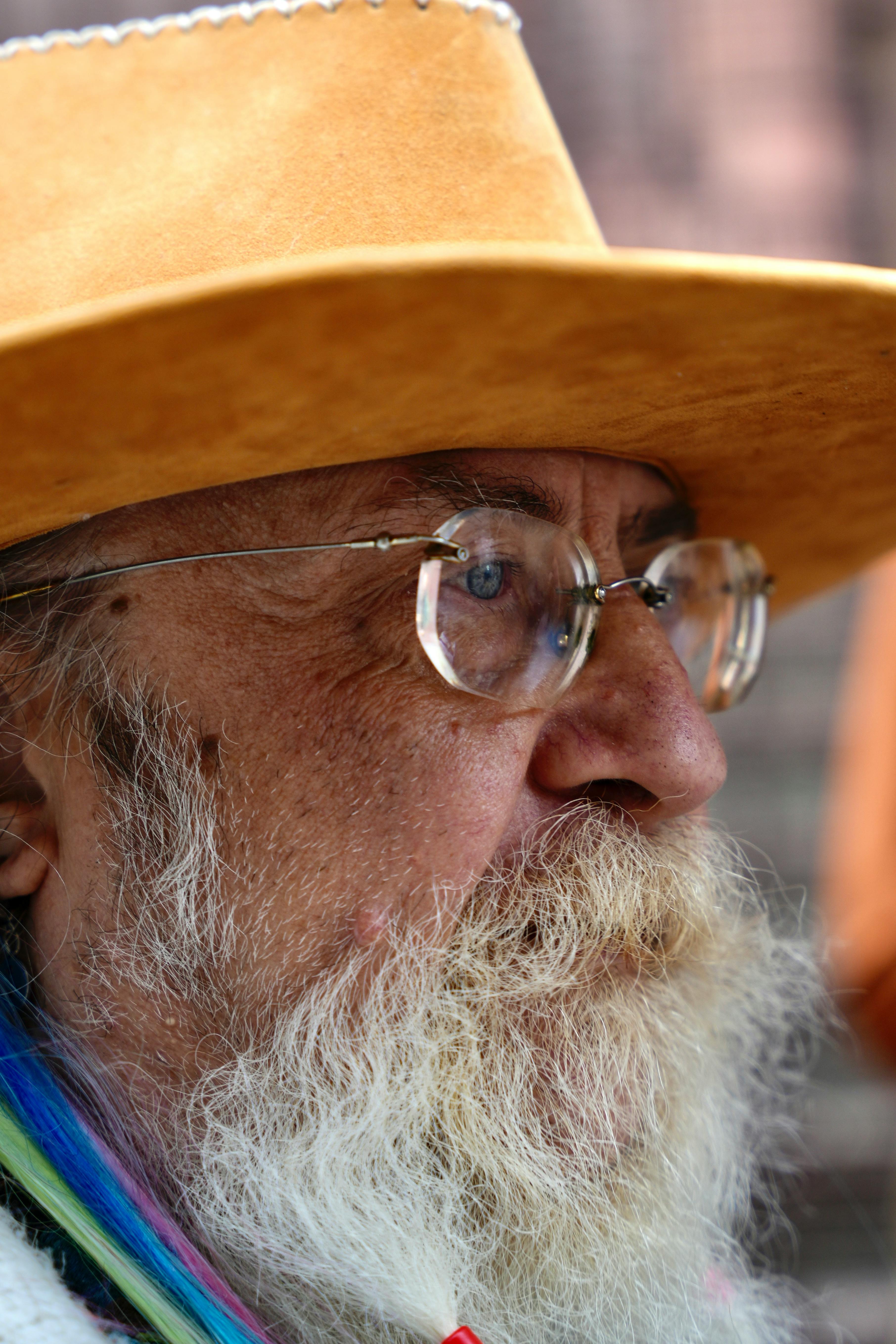 Close-up portrait of an elderly man with a hat, glasses, and beard, showcasing wisdom and character.