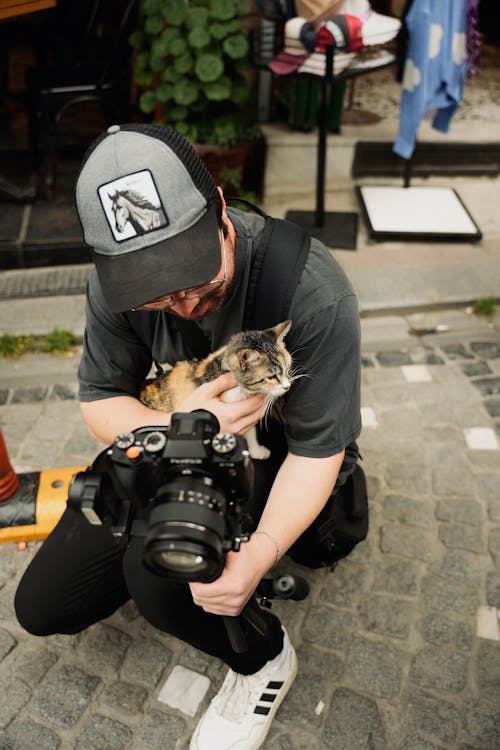 Man in Cap and with Camera Squatting and Holding Kitten