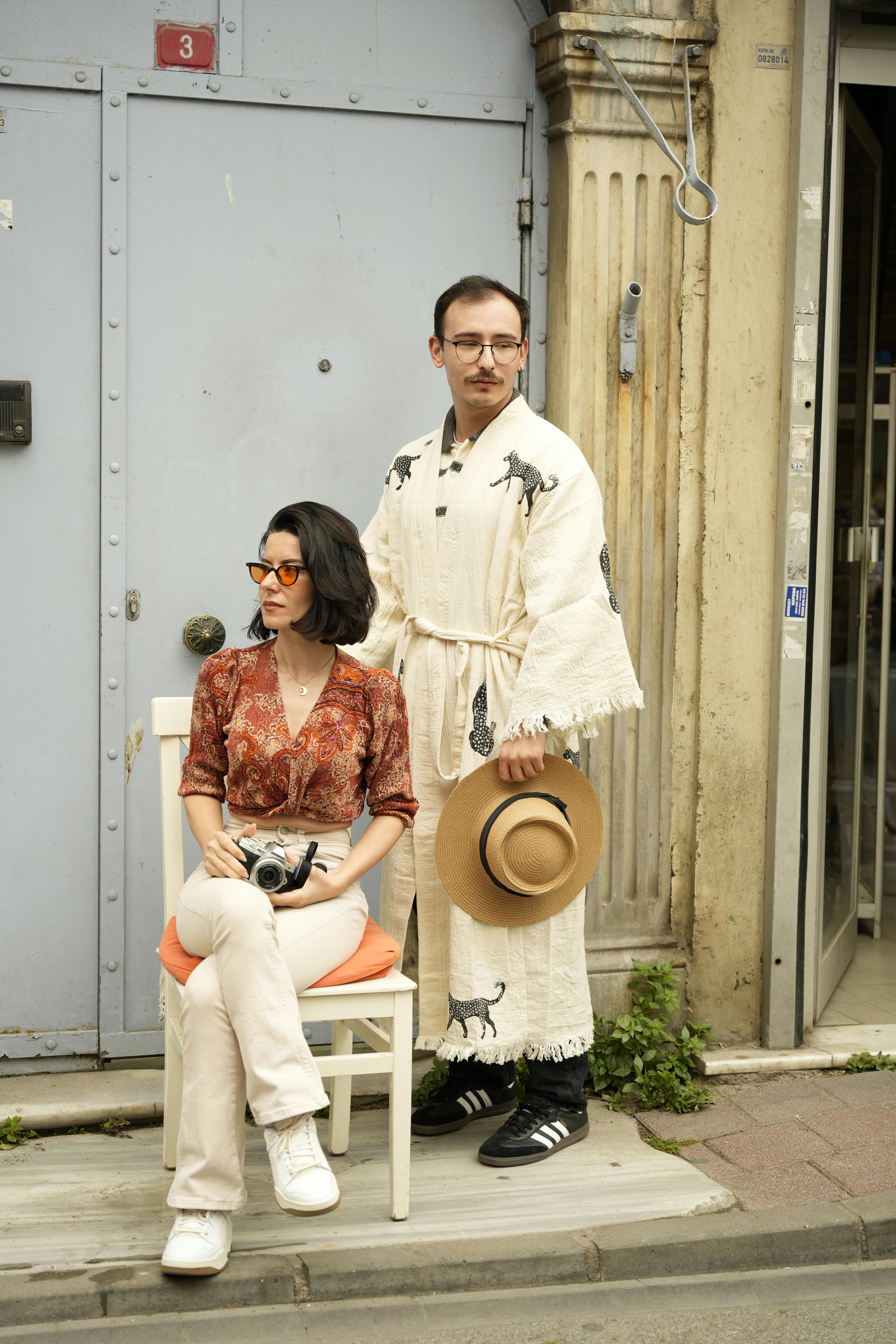 A fashionable couple poses with vintage outfits in an urban setting, blending traditional and modern styles.