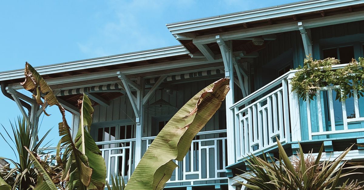 Photo by Vincent Rivaud Tropical-themed wooden house with lush foliage and vibrant balcony under clear skies.