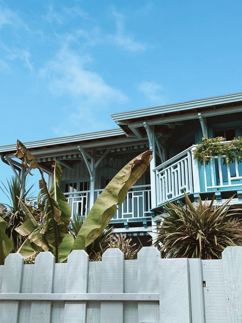 Photo by Vincent Rivaud Tropical-themed wooden house with lush foliage and vibrant balcony under clear skies.