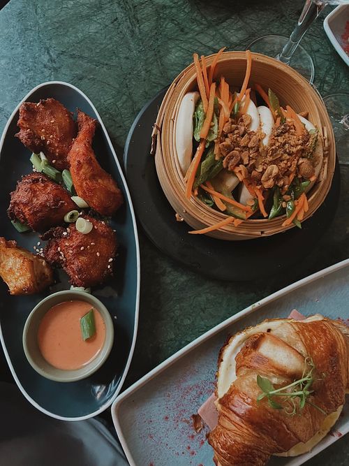 Free High angle view of gourmet dishes including chicken wings, bao buns, and a croissant sandwich. Stock Photo
