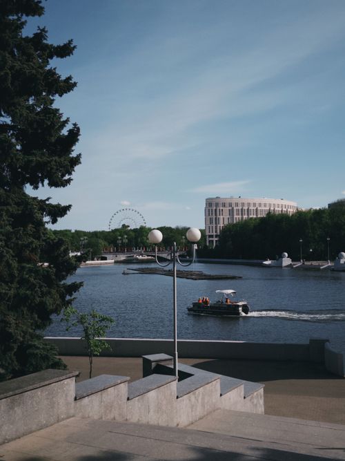Free Discover a picturesque view of the Svislach River with a motorboat, lush trees, and urban landscape in Minsk, Belarus. Stock Photo
