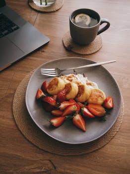 A tempting breakfast spread with pancakes, strawberries, and tea on a wooden table.