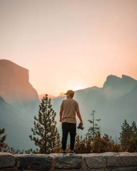 一名男子手持相机，站在那里凝视着雄伟的山上日出，拥抱孤独和大自然的美丽