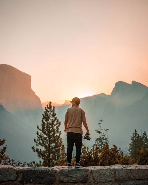 Free A man stands gazing at a majestic mountain sunrise, holding a camera, embracing solitude and nature's beauty. Stock Photo