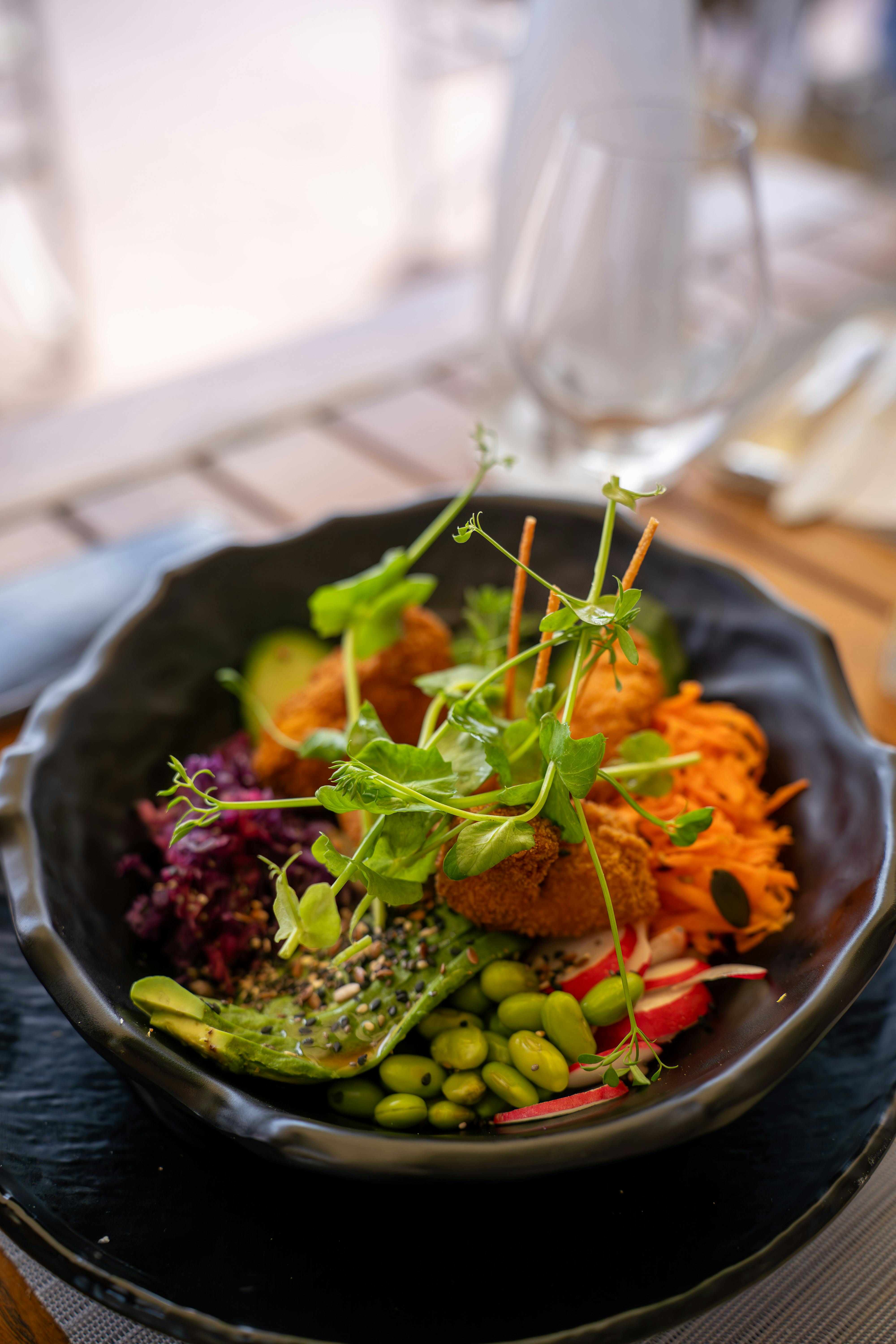 Colorful vegetarian bowl with fresh vegetables and herbs in a black bowl on a wooden table.