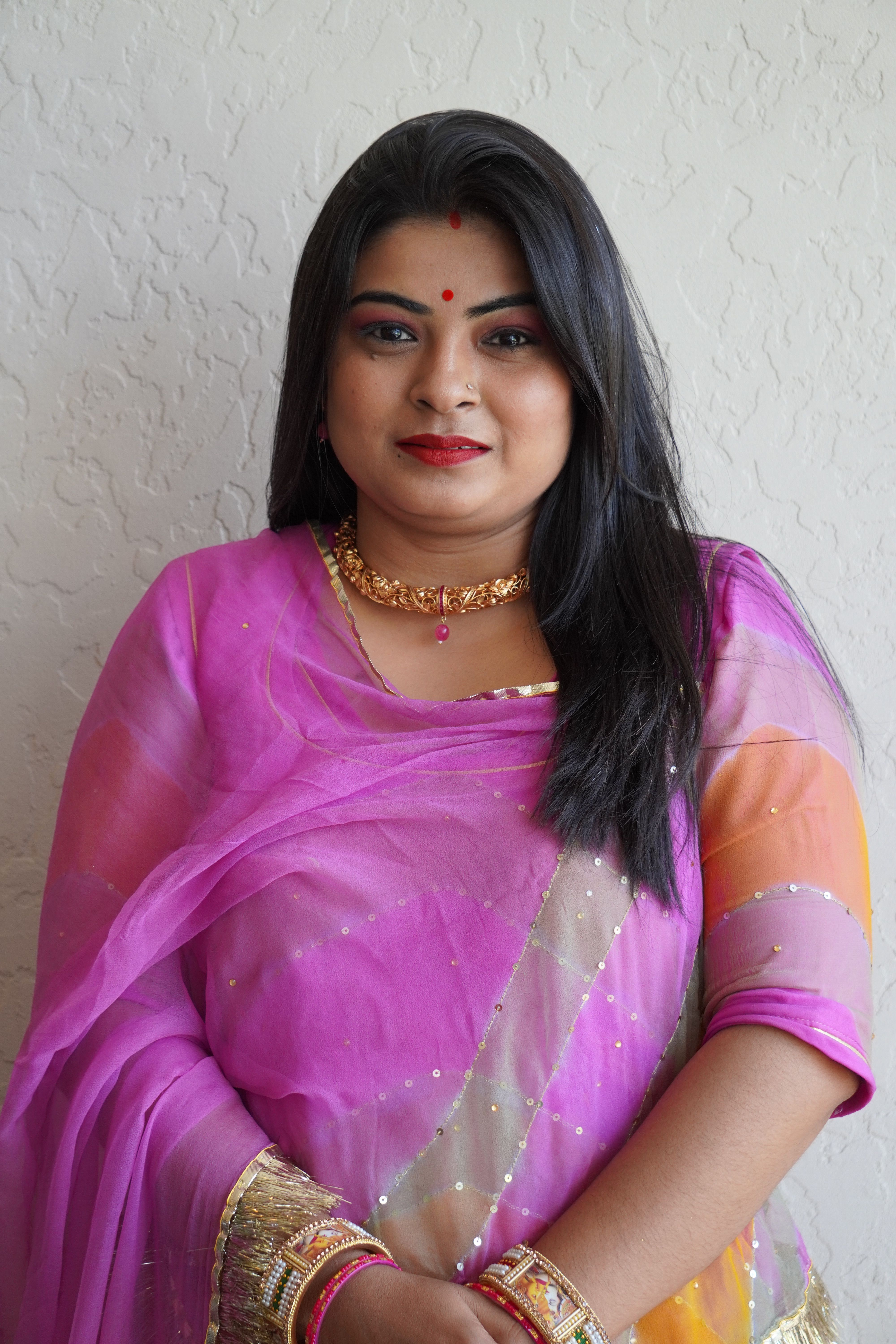 A woman wearing a traditional pink sari and gold jewelry, posing gracefully and smiling.
