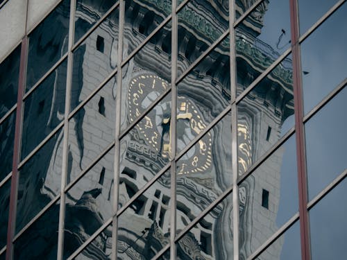 A clock tower reflected in a building's windows