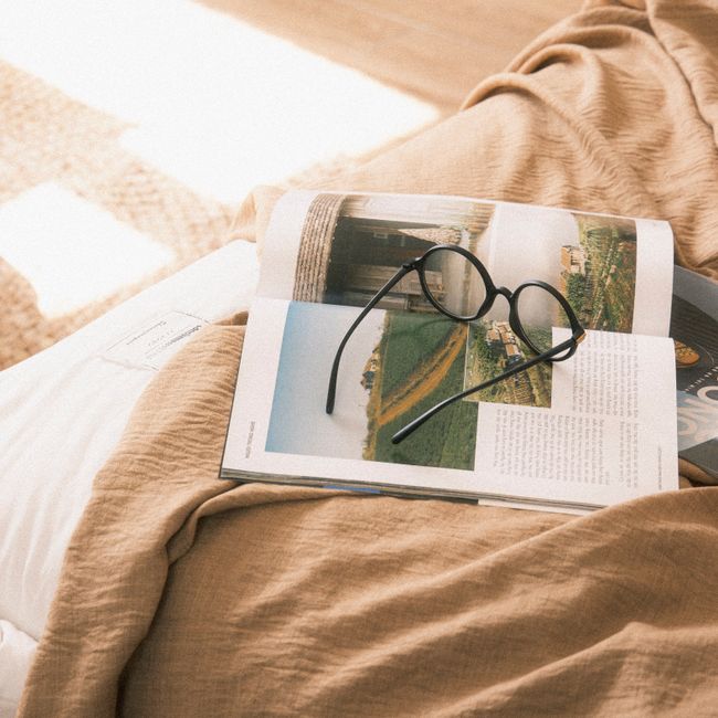 A pair of eyeglasses resting on an open book on a cozy bed, basked in gentle sunlight.