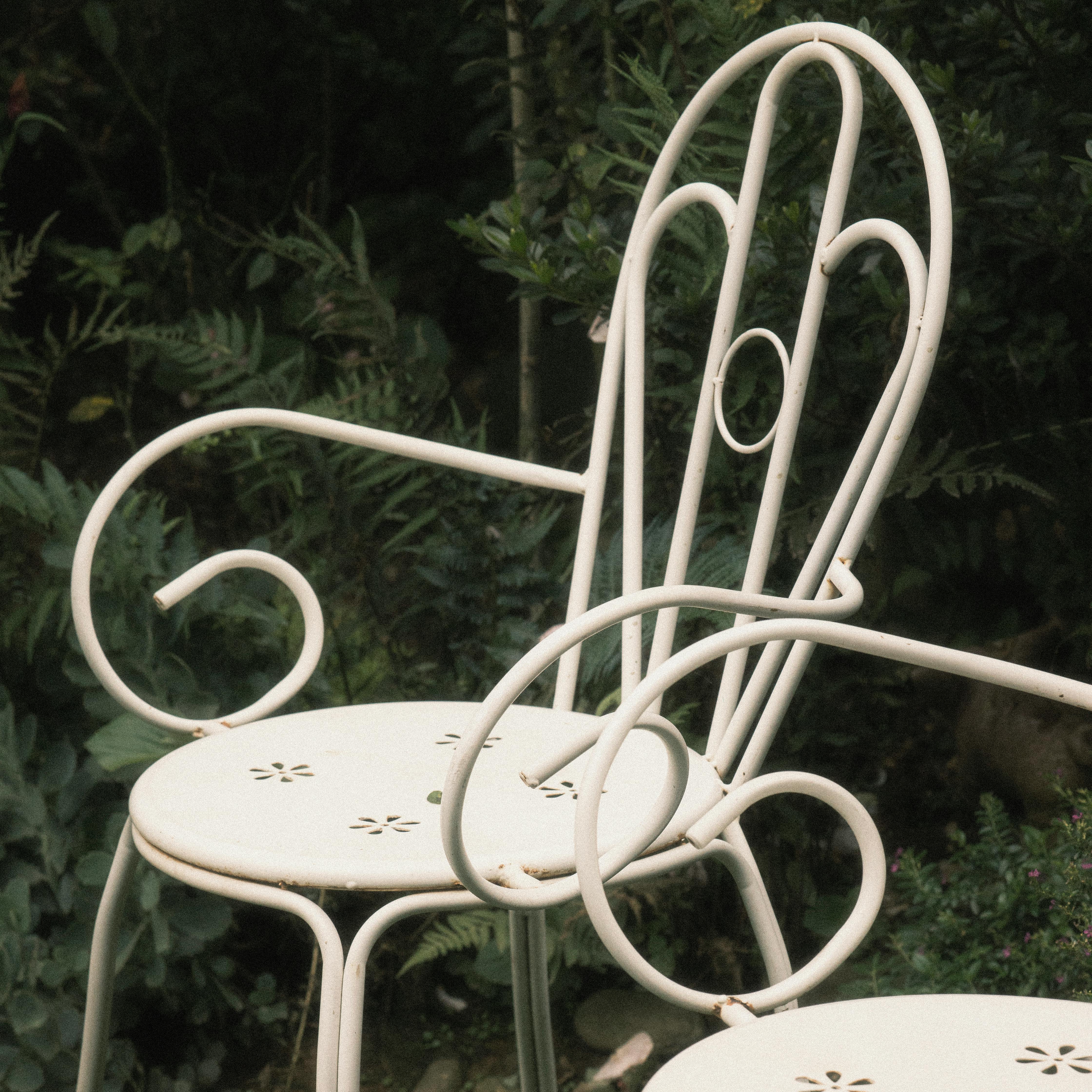 Ornate white metal chairs in a lush garden setting. Perfect for outdoors and patio decor.