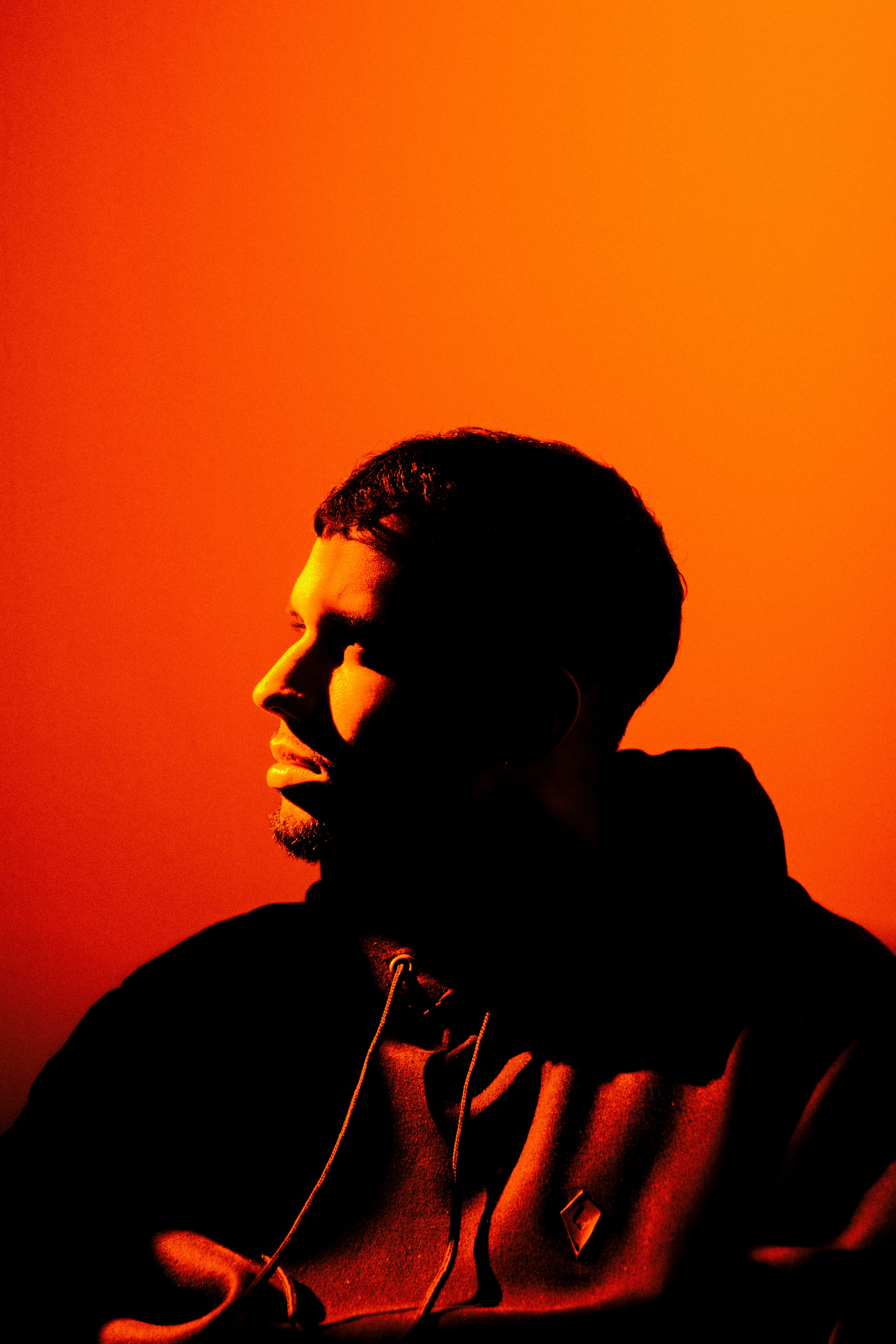 Portrait of a man in dramatic lighting with a warm orange background.