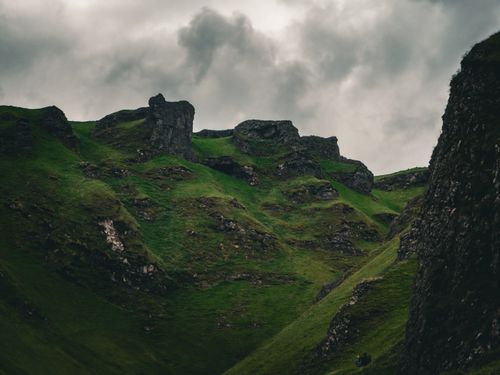 Free A scenic view of lush green hills with rocky outcrops under a dramatic cloudy sky, creating a moody atmosphere. Stock Photo