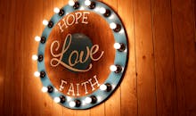 木墙上的灯泡照亮了一个充满活力的圆形标志，上面写着“希望、爱、信仰”