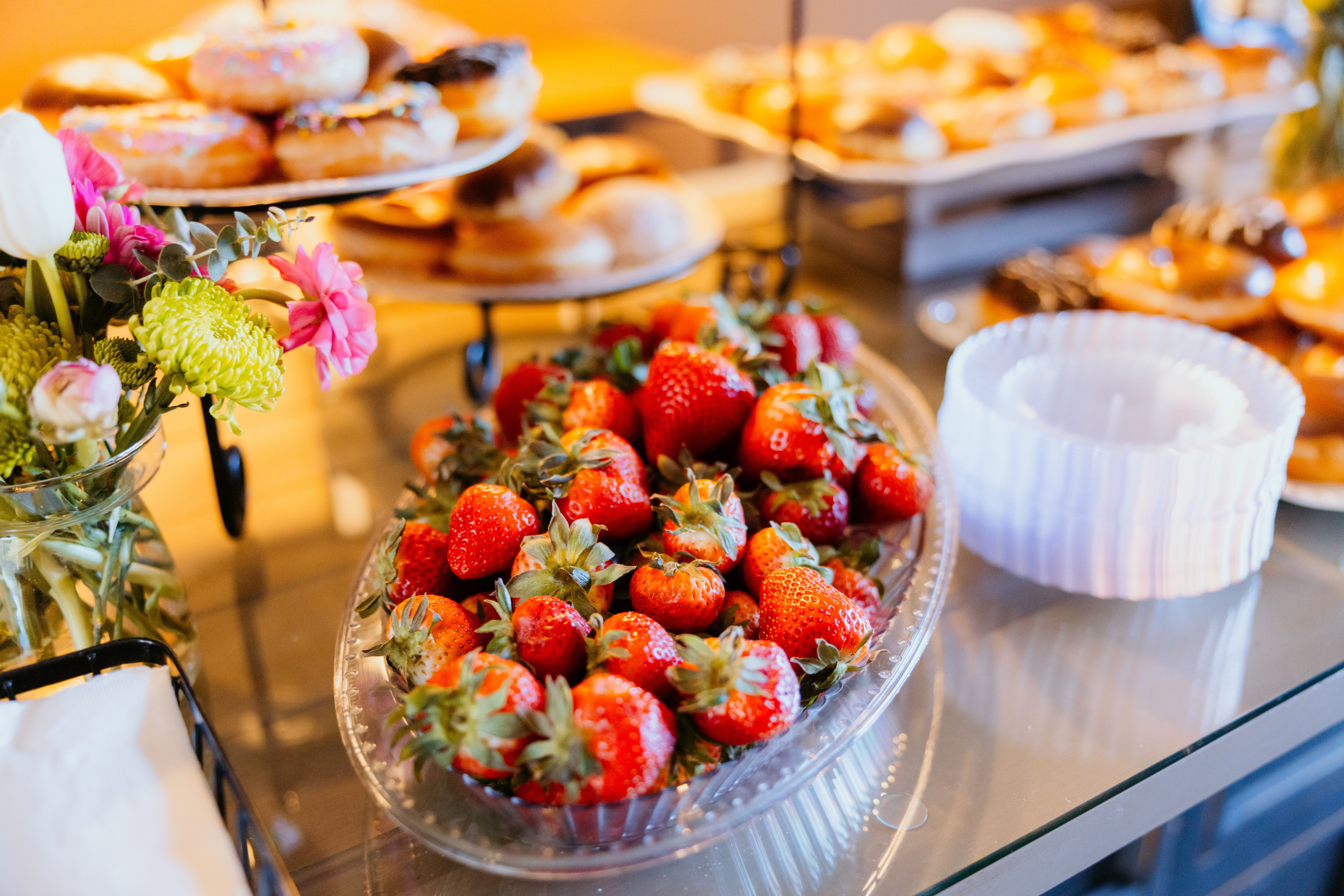 A colorful buffet spread featuring fresh strawberries, donuts, and floral decorations.