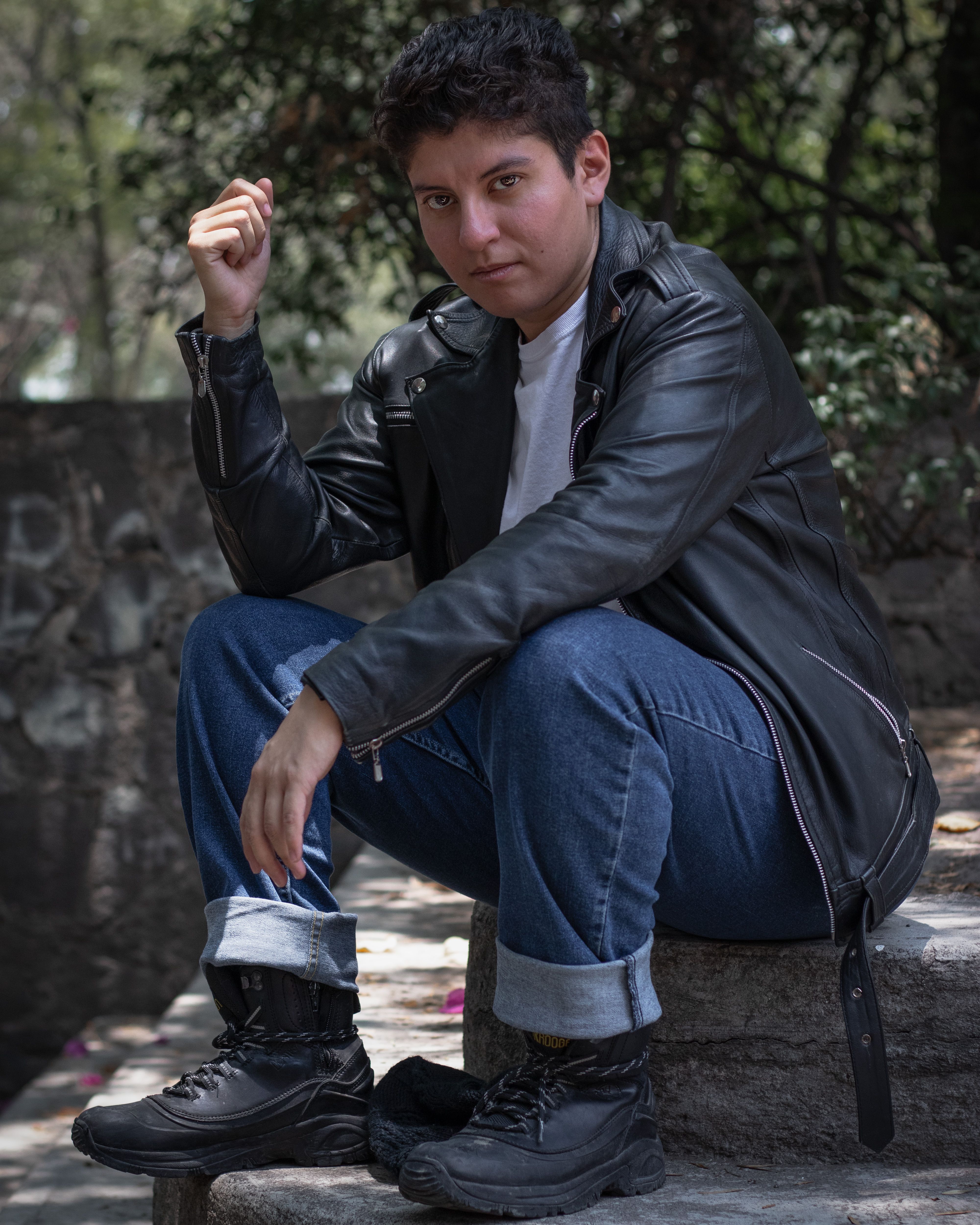 Young man poses confidently in Ciudad de México wearing a leather jacket and jeans.