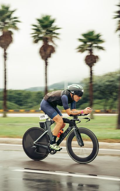 A cyclist races in a tropical outdoor time trial event with palm trees in the background.