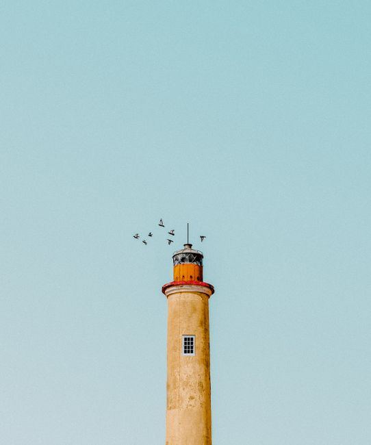 A lighthouse with a clear blue sky and birds flying above in Curaçao.