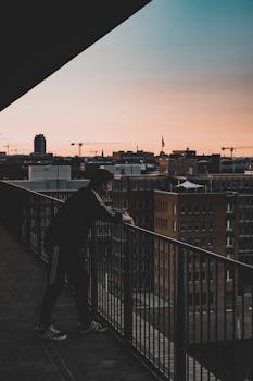 日落时分，一名身穿休闲装的男子在高层阳台上眺望城市景观