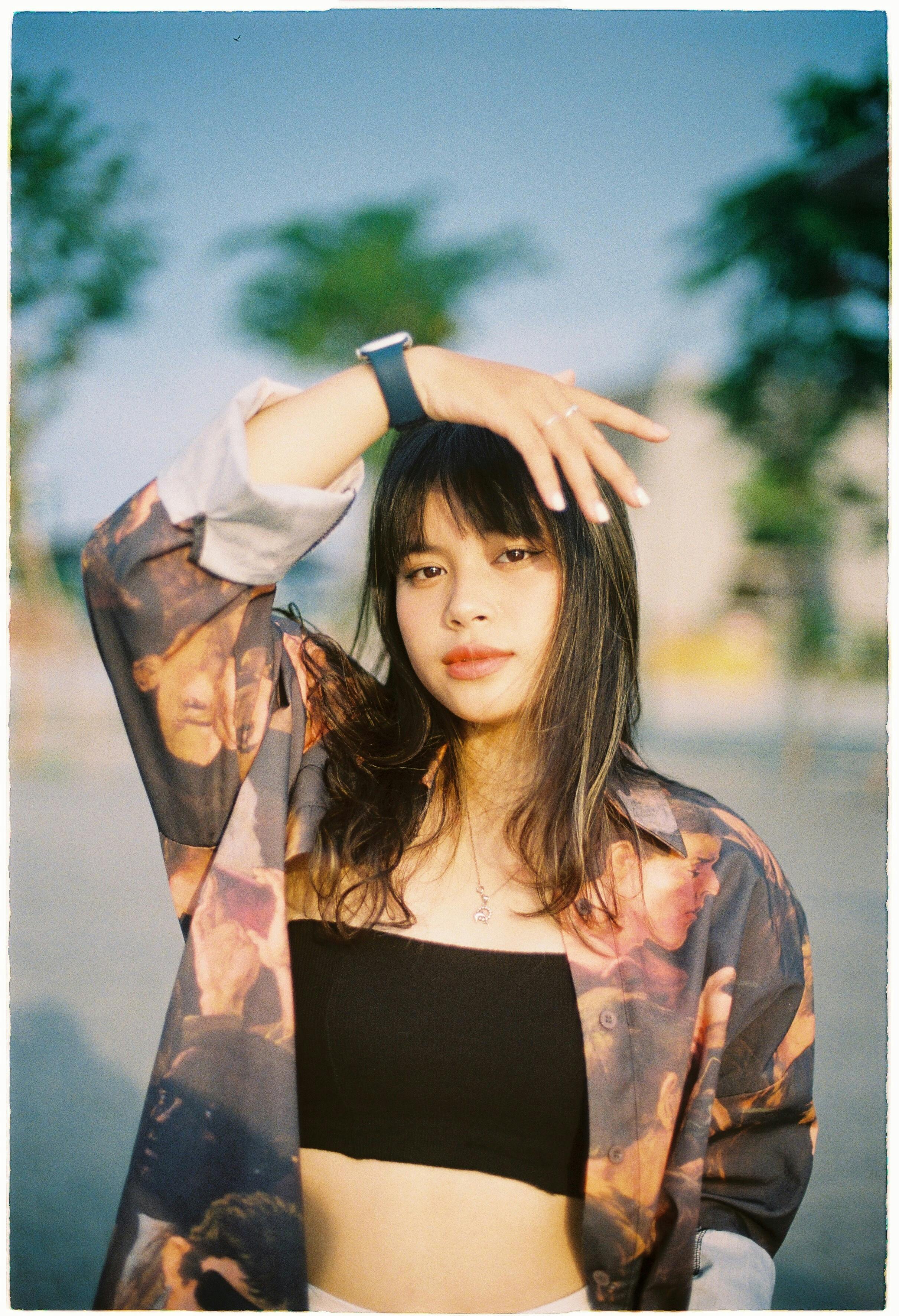 Portrait of a young woman outdoors in a black top and artistic jacket, wearing a wristwatch.