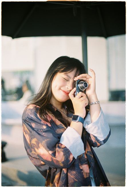 Young Asian woman with a vintage camera enjoying photography outdoors, smiling tenderly.