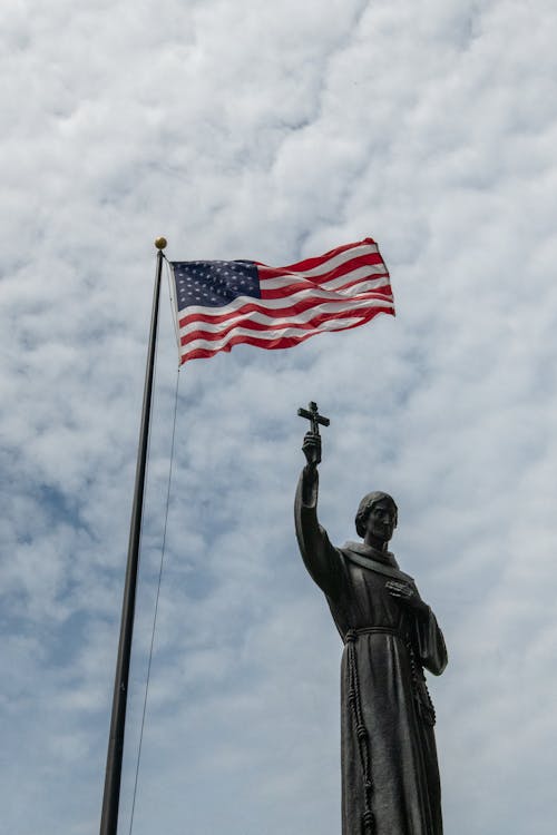 A statue of st francis of assisi is seen in front of the us flag